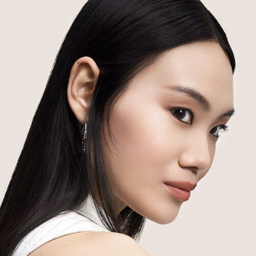 Portrat einer Frau mit langen, glatten Haaren, die leicht zur Seite schaut; neutraler Hintergrund.