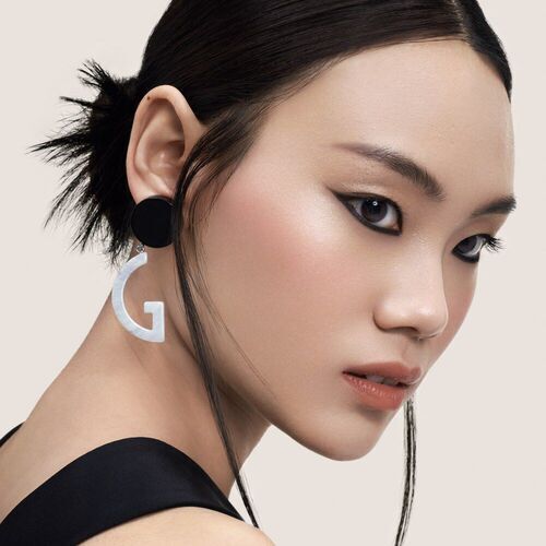 Portrat einer Frau mit elegantem Make-up und auffalligem Ohrring in Form eines Buchstabens „G“.