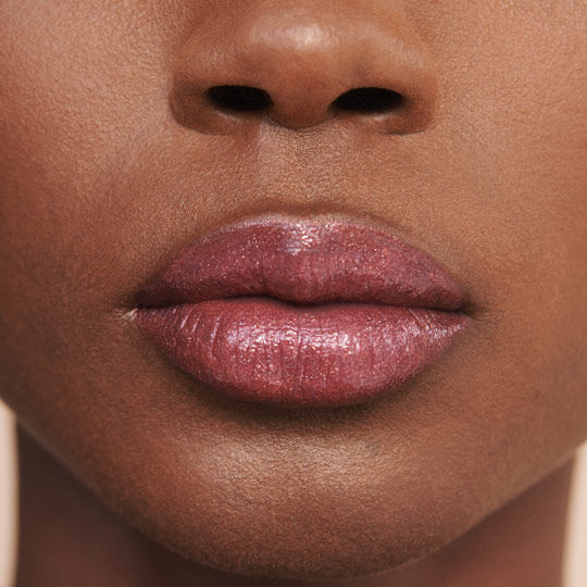 Close-up of a person's lips with a glossy, rosy sheen, set against a neutral background.