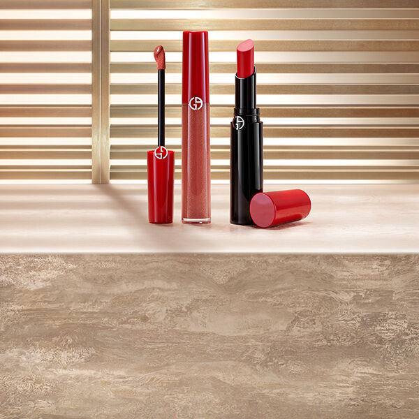 Roter Flussiglippenstift und roter Lippenstift von Giorgio Armani auf einer Steinoberflache vor sonnenbeschienenen Jalousien.