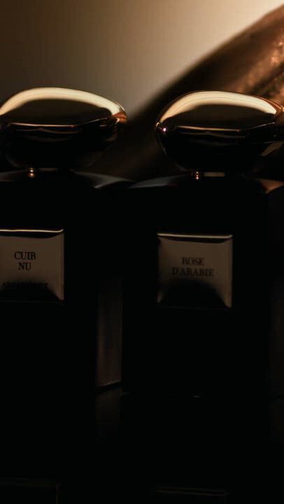 Three dark Armani/Prive fragrance bottles with gold caps are showcased with labels "Oud Royal", "Cuir Nu", and "Rose d'Arabie." The video includes close-ups of vanilla pods, shimmering wood, and a golden fig, emphasizing luxurious, warm, and exotic notes.