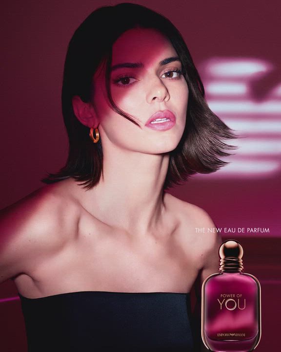 Eine Anzeige fur das „Power of You“ Eau de Parfum von Emporio Armani. Das Bild zeigt das Model Kendall Jenner auf der linken Seite, die mit einem sanften Ausdruck in die Kamera blickt. Sie hat kurzes dunkles Haar und tragt ein schwarzes tragerloses Oberteil sowie goldene Creolen. Auf der rechten Seite ist ein tiefrosa-lilafarbener Parfumflakon mit der Aufschrift „Power of You“ und „Emporio Armani“ zu sehen. Im Hintergrund leuchtet ein stilisiertes Armani-Adler-Logo vor einem dunkelmagentafarbenen Hintergrund. Der Text lautet „POWER OF YOU“ oben rechts und „THE NEW EAU DE PARFUM“ unten rechts.