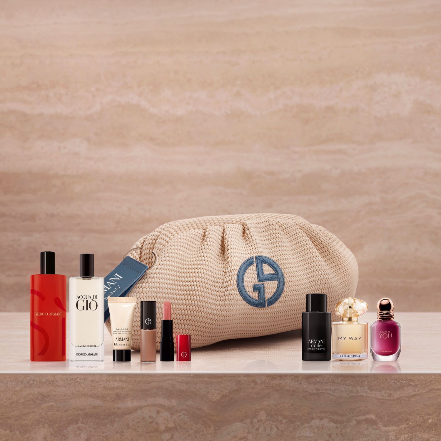 Eine luxuriose Auswahl an Armani-Ikonen: die Dufte Si, Acqua di Gio und My Way, neben Luminous Silk Foundation und einem Lippenstift. Elegant arrangiert auf Marmor mit einer beigen Flechtpochette, feiert diese Kollektion edle Couture-Schonheit.