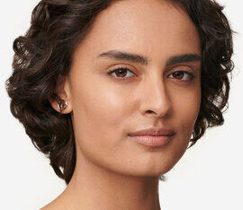 A close-up portrait of a person with short, curly hair and a natural makeup look, gazing confidently at the camera.