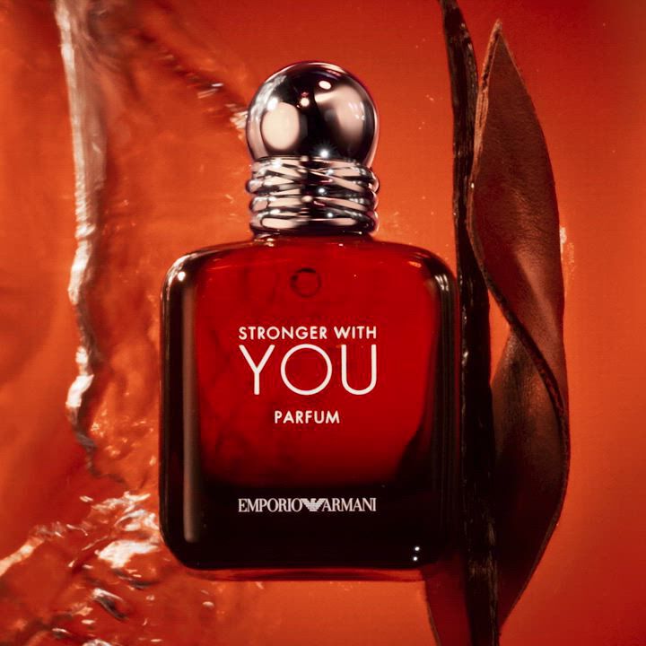 A dark amber glass perfume bottle labeled "Stronger With You Parfum" by Emporio Armani, set against a vibrant orange background with soft waves of texture.