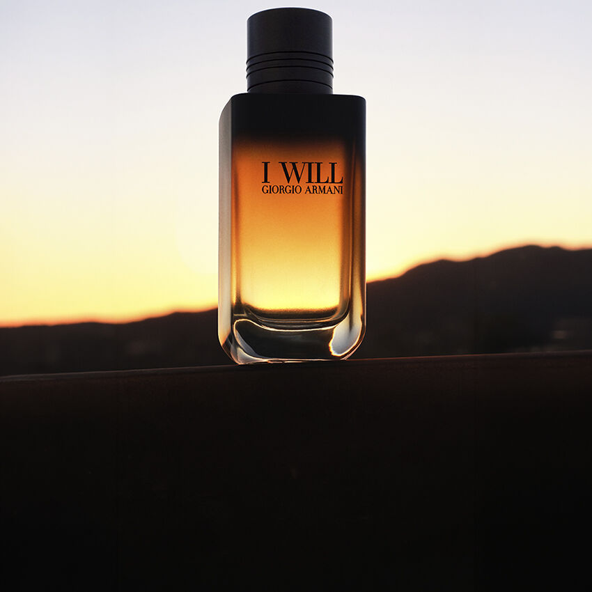 Flakon des Duftes I WILL von Giorgio Armani vor einer Landschaft bei Sonnenuntergang.