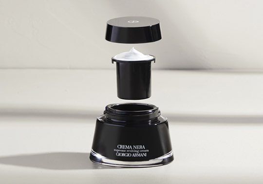 A black jar of Giorgio Armani's Crema Nera Supreme Reviving Cream, with the lid and inner container slightly lifted to reveal the white cream inside.