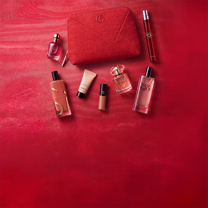 Drei Armani Beauty Produkte — ein Lippenprodukt, der Duft Power of You und die Luminous Silk Foundation — vor einem strukturierten roten Hintergrund.