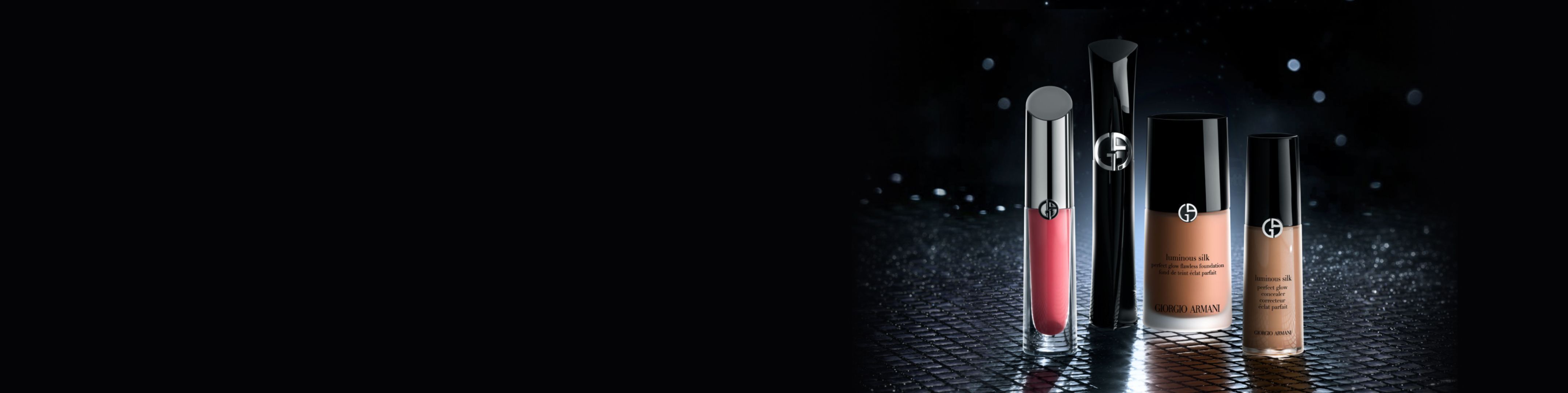 Armani-Beauty-Make-up vor dunklem Hintergrund: roter Lippenlack, schwarze Mascara, Luminous Silk Foundation und Concealer auf einer reflektierenden Flache.