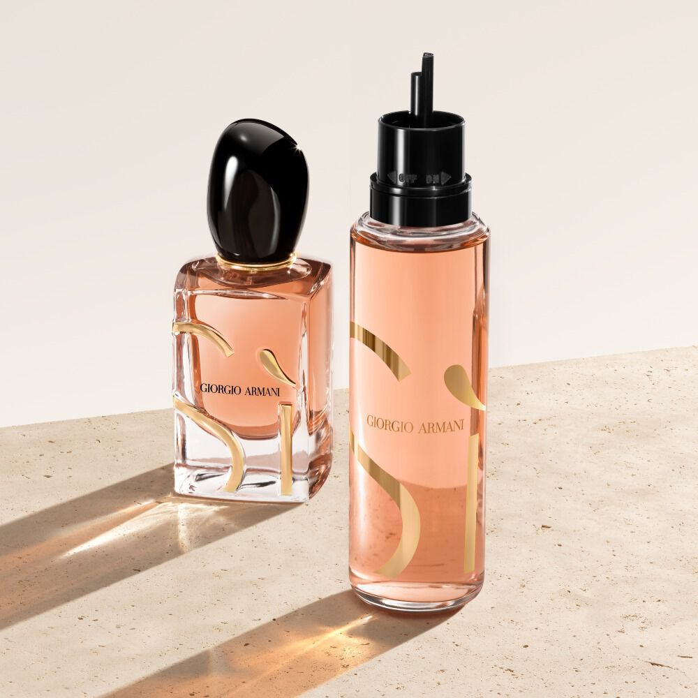 Zwei Flakons Giorgio Armani Si Eau de Parfum stehen auf einer beigen Oberflache. Links der klassische Si Parfumflakon, rechts daneben ein Nachfullflakon mit durchscheinenderem pfirsichfarbenem Aussehen.