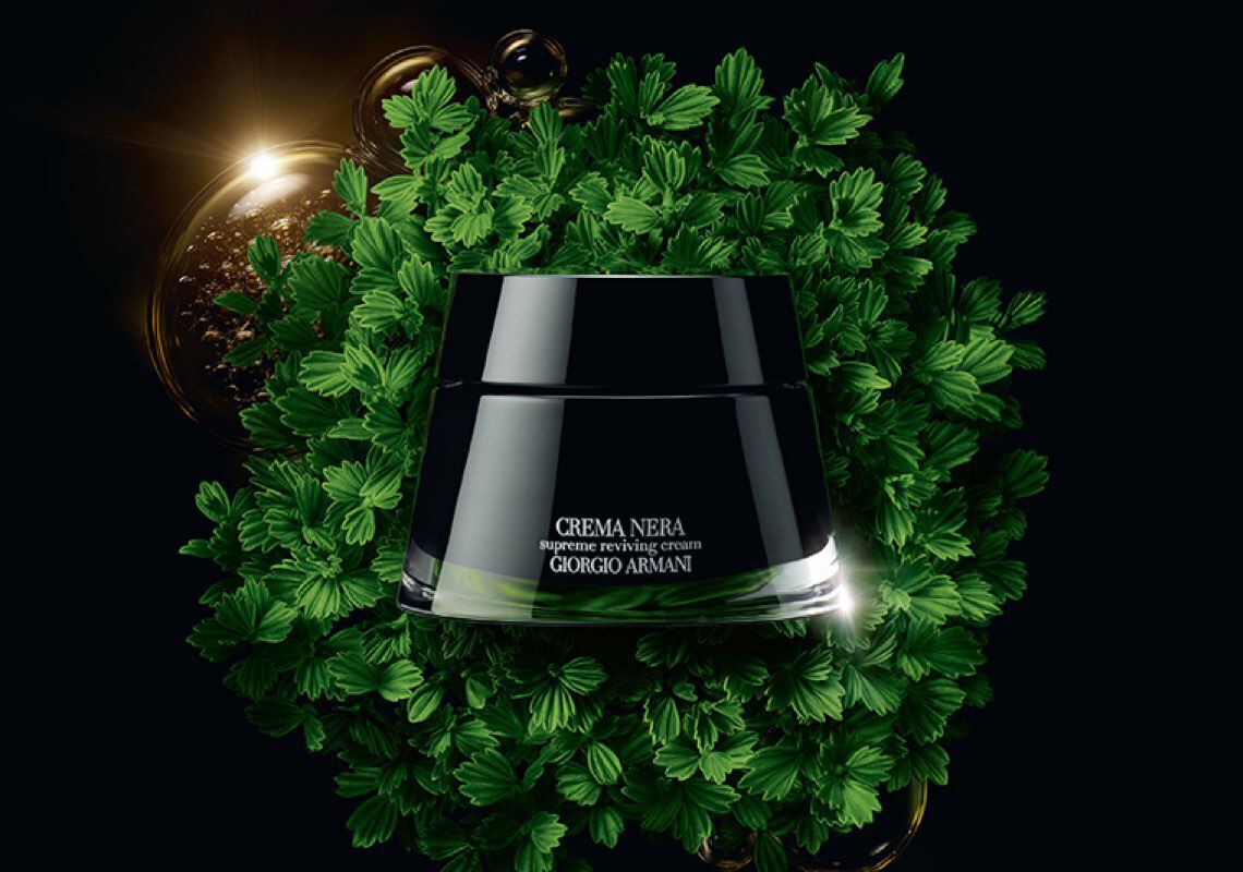 A jar of Giorgio Armani's Crema Nera Supremes Reviving Cream surrounded by lush green leaves and a glowing background.