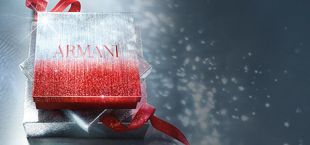 Armani Geschenkbox in glitzerndem Rot und Silber mit rotem Band, vor einem schimmernden Hintergrund.