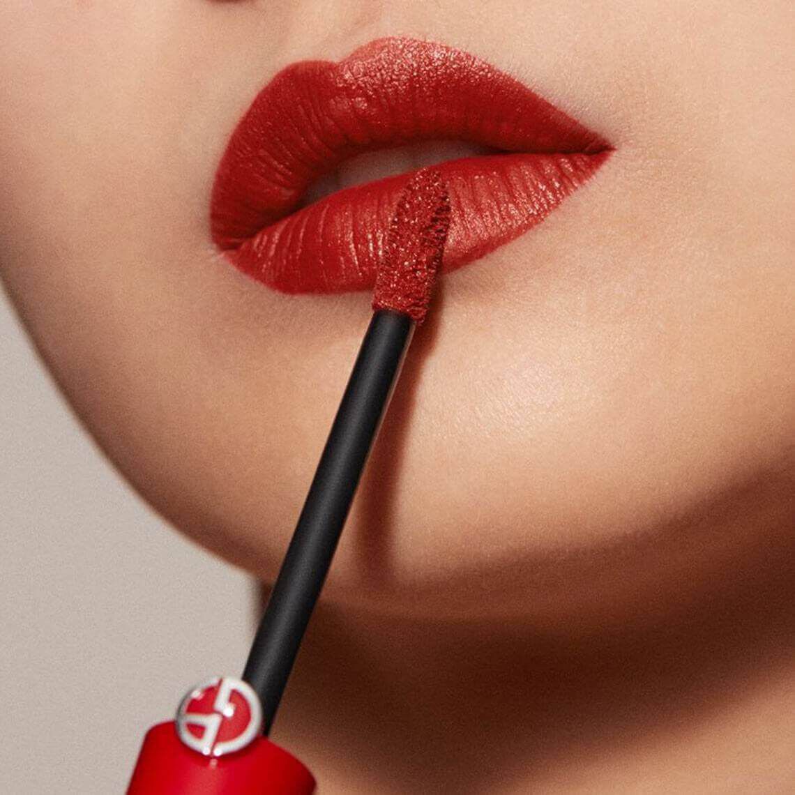 Close-up of a person's lips adorned with a rich red lipstick, with a wand applicator nearby.