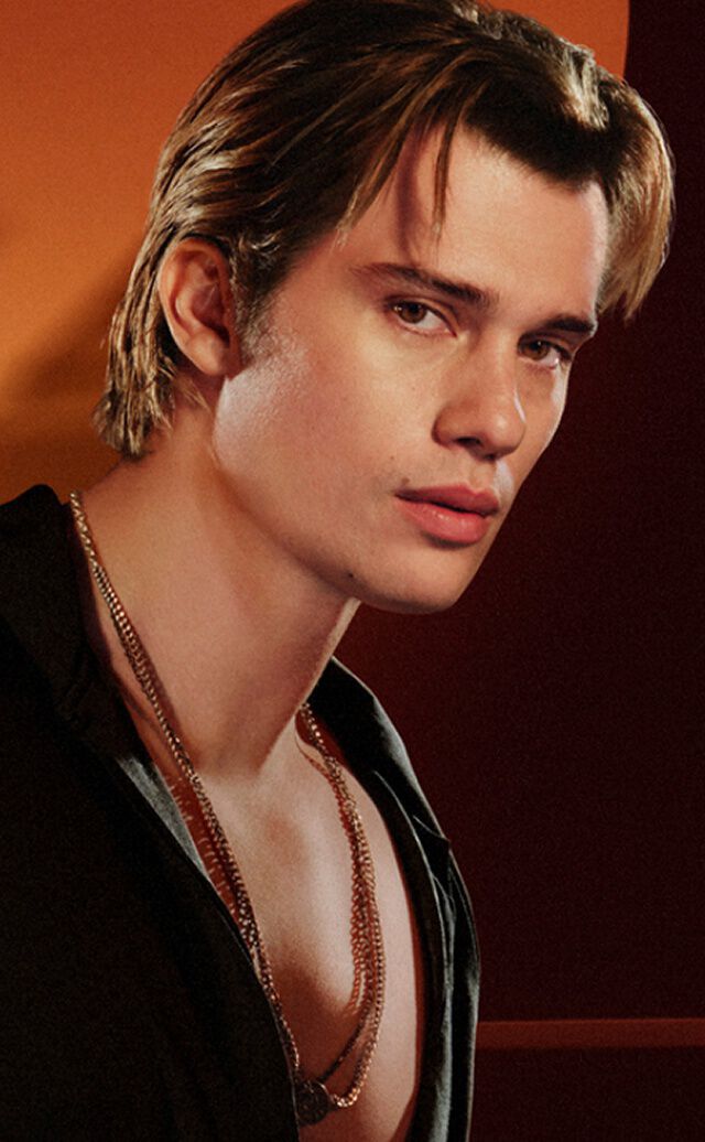 Eine Anzeige fur die „Stronger With You“ Duftserie von Emporio Armani. Auf der linken Seite tragt ein junger Mann mit hellbraunem Haar ein schwarzes Hemd und silberne Halsketten und blickt mit ernstem Blick in die Kamera. Auf der rechten Seite zeigt ein Produktkarussell unter dem Titel „EVERY FACET OF STRONGER WITH YOU“ drei verschiedene Parfumflakons. Der mittlere, hervorgehobene Flakon ist „Stronger With You Powerfully“ in der 50-ml-Große zum Preis von 74,00 £, mit einer Schaltflache „IN DEN WARENKORB“ darunter. Navigationspfeile und ein Schieberegler sind ebenfalls sichtbar.