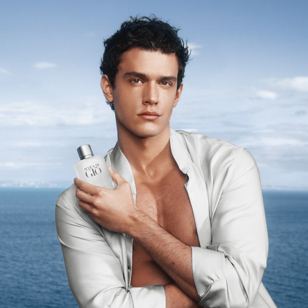 A model holding the iconic Armani beauty Acqua di Gio men's fragrance. Set against a luminous sea and sky backdrop, embodying the natural and refined essence of the classic Eau de Toilette.