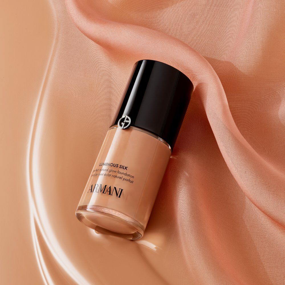 A bottle of newly enhanced Armani beauty Luminous Silk Foundation with its black cap, placed on a flowing, silky pink fabric, highlighting the product's iconic status and luxurious feel.