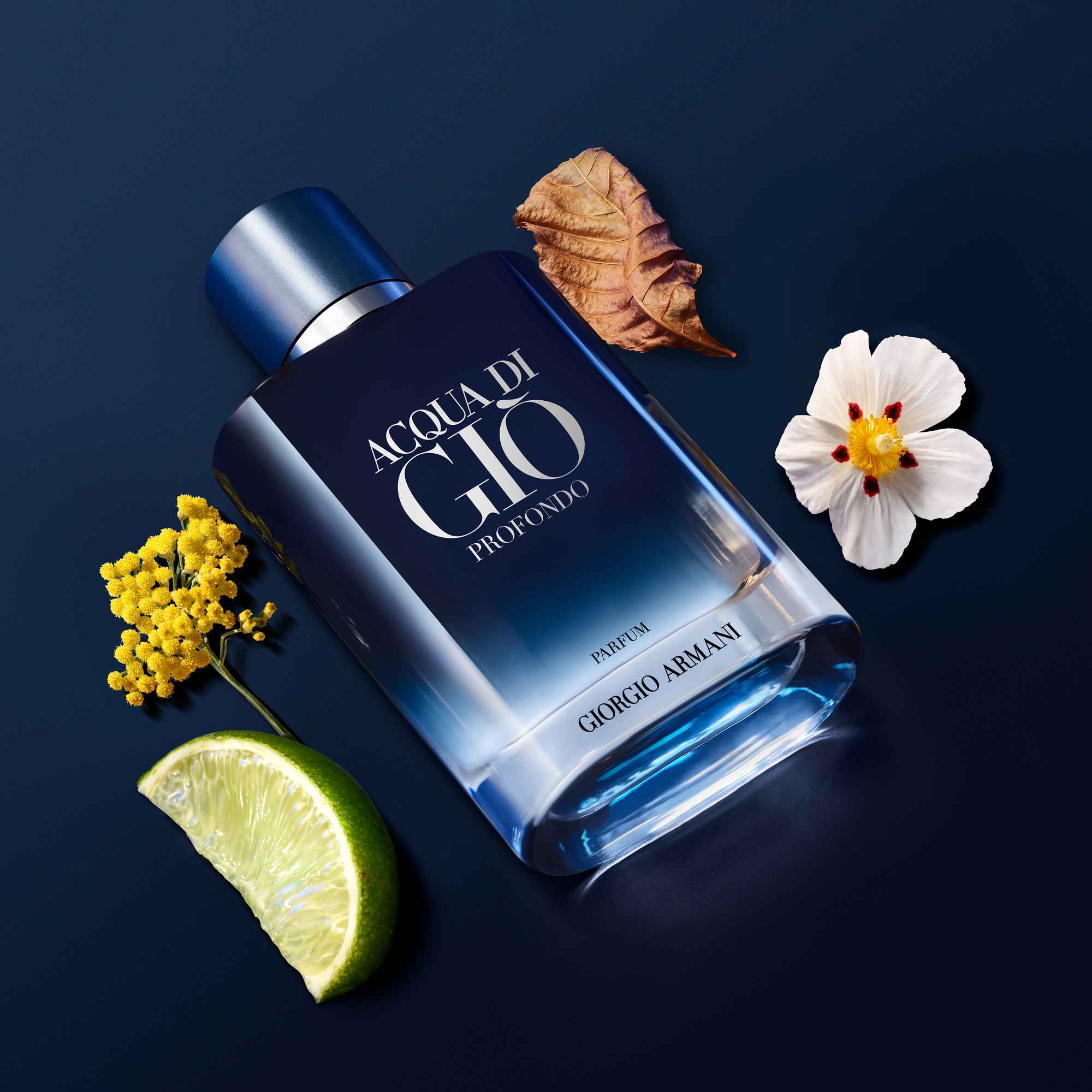 Flasche von Acqua di Gio Profondo von Giorgio Armani, umgeben von Blumen, Blättern und Limettenscheibe auf blauem Hintergrund.
