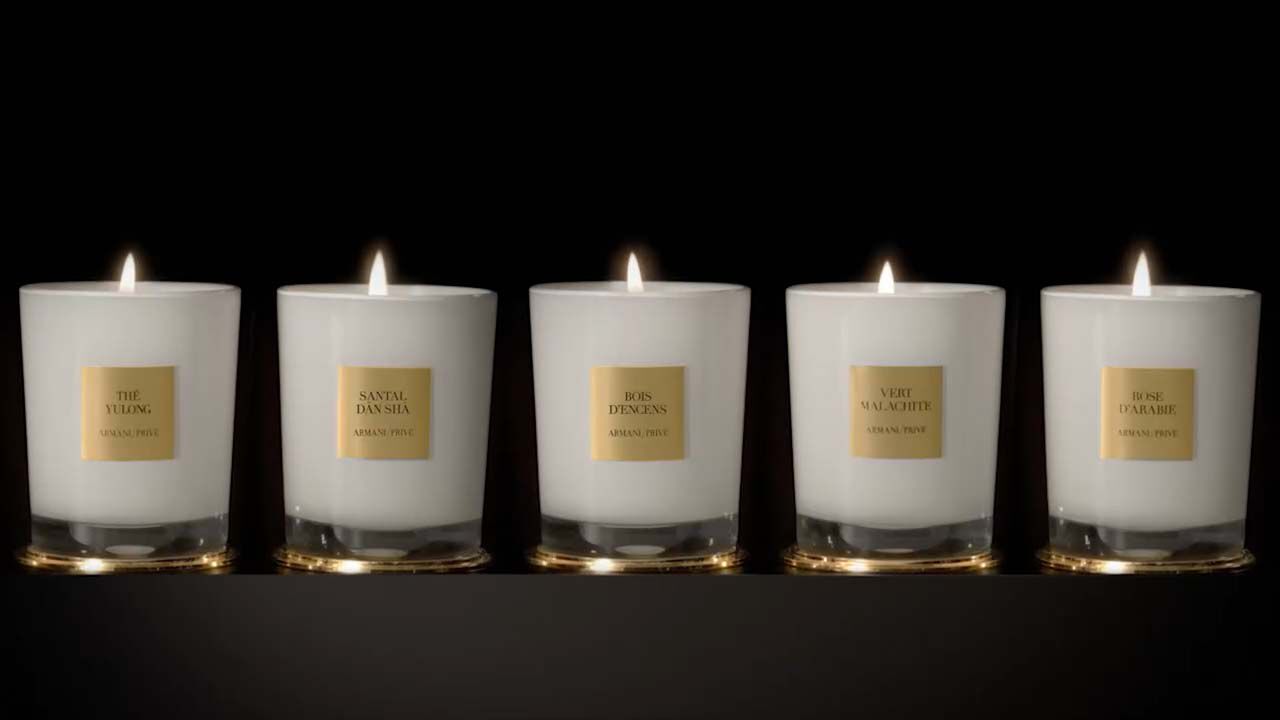 Fünf elegante Duftkerzen in Glasbehältern mit goldenen Etiketten auf schwarzem Hintergrund.