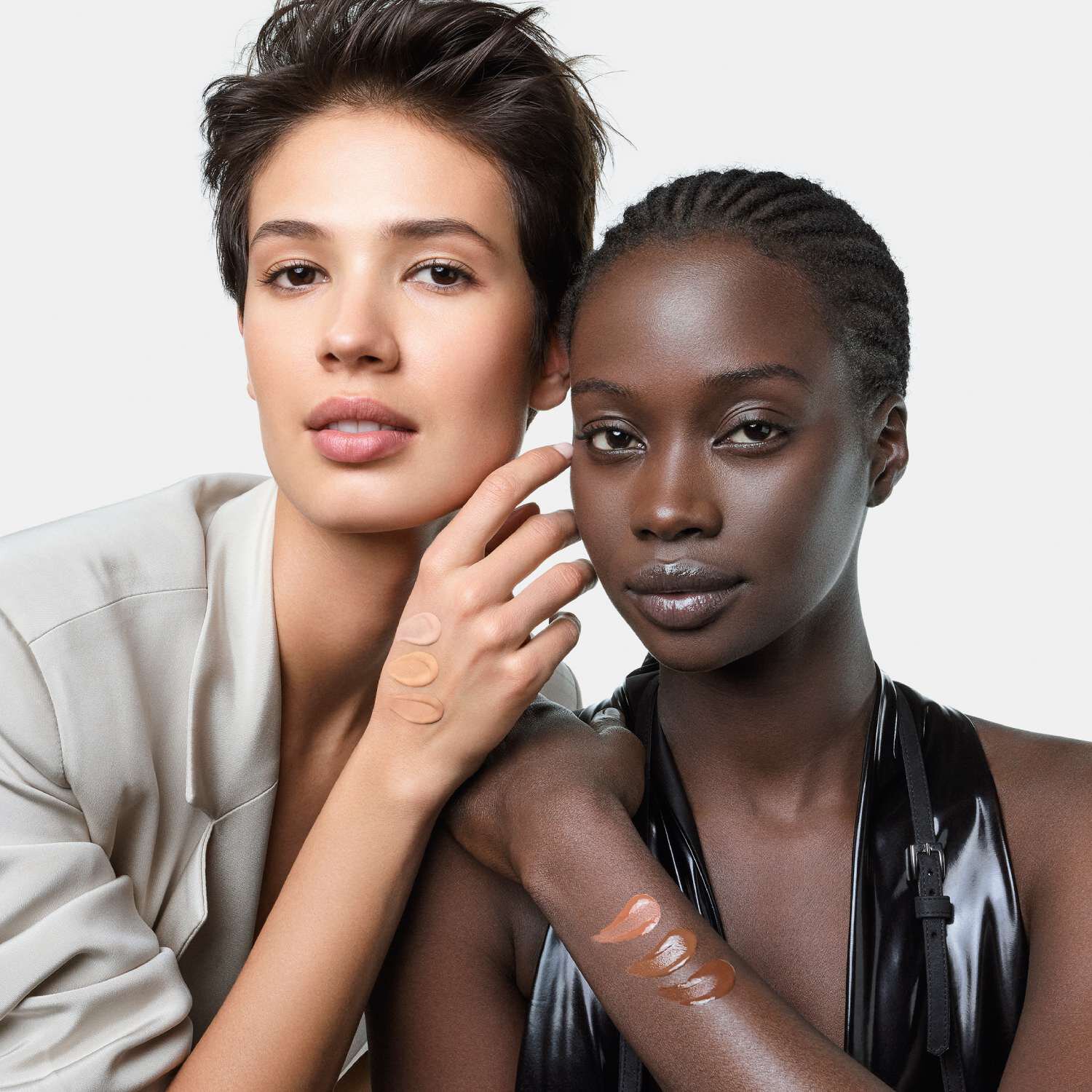 Two people show foundation swatches on their arms across different skin tones.close-up of a model applying foundation with a brush, holding Giorgio Armani foundation in front of her face.